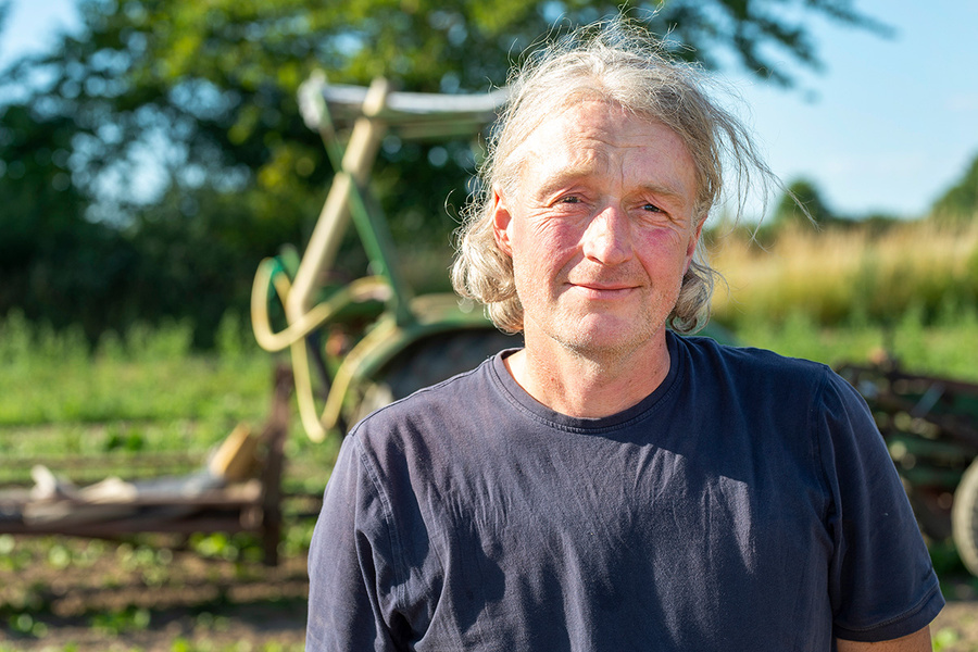 KI generiert: Ein Mann steht auf einem Feld vor einem Traktor im Sonnenschein.