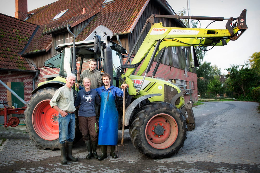 KI generiert: Vier Personen stehen vor einem Traktor auf einem Bauernhof.
