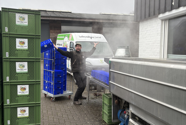 KI generiert: Ein Mann steht fröhlich vor einem Lieferwagen mit der Aufschrift "Lebendiges Land" neben grünen Kisten.