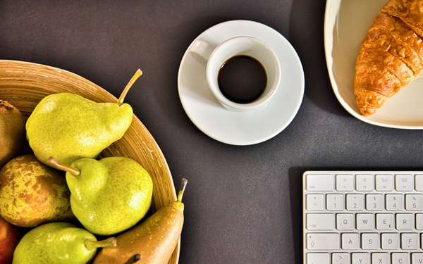 KI generiert: Korb mit Birnen, Tasse Kaffee, Croissant und Computertastatur auf dunklem Hintergrund.