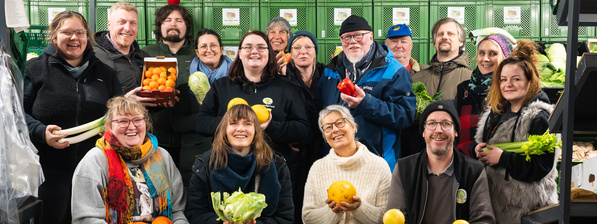 Unser Team: eine fröhliche Gruppe von Menschen präsentiert frisches Obst und Gemüse.