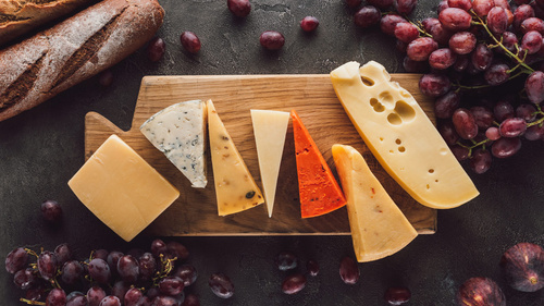 KI generiert: Verschiedene Käsesorten auf einem Holzbrett, umgeben von Trauben und Baguette.