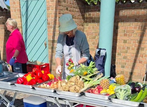 KI generiert: Eine Person arrangiert Gemüse und Obst an einem Marktstand im Freien.