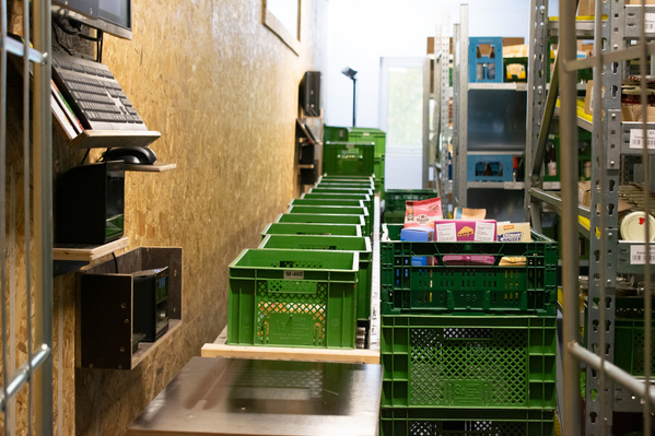 KI generiert: Grüne Kisten in einer Lagerhalle, mit Konsumgütern gefüllt, auf Regalen gestapelt.