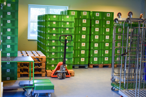 KI generiert: Grüne Kisten stapeln sich in einem Lagerraum mit Paletten und einem Hubwagen.