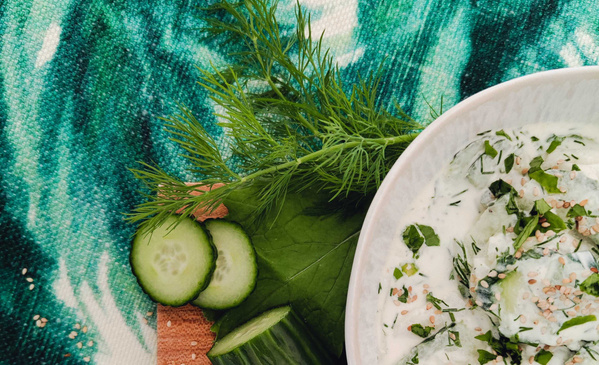 KI generiert: Ein Schälchen mit Gurkensalat, garniert mit Dill und frischen Kräutern auf einem grünen Tuch.