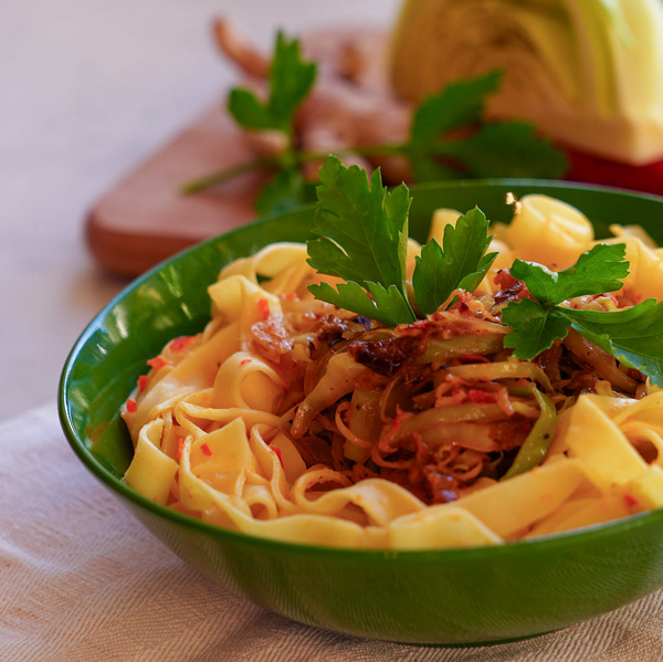 KI generiert: Grüner Teller mit Pasta, garniert mit Petersilie und Gemüse, im Vordergrund.