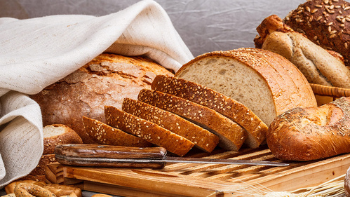KI generiert: Verschiedene Brotsorten auf einem Holzbrett, darunter geschnittenes Brot und ein Messer.