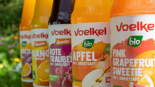 KI generiert: Mehrere Flaschen mit verschiedenen Voelkel Fruchtsäften. Texte: "Voelkel", "bio", "100% Direktsaft".
