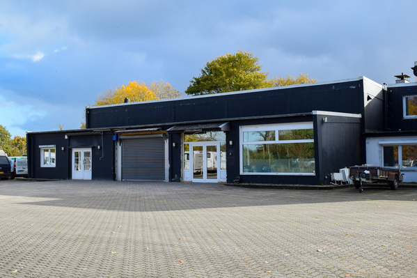 KI generiert: Ein graues Industriegebäude mit großem Rolltor und gepflastertem Vorplatz.