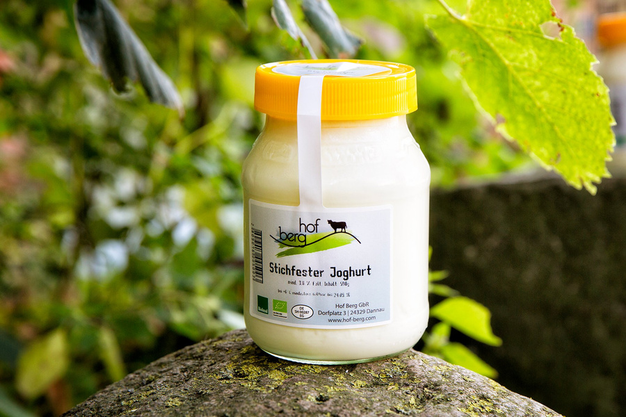 KI generiert: Ein Glas stichfester Joghurt von Hof Berg mit gelbem Deckel im Freien. Text: "hof berg, Stichfester Joghurt."