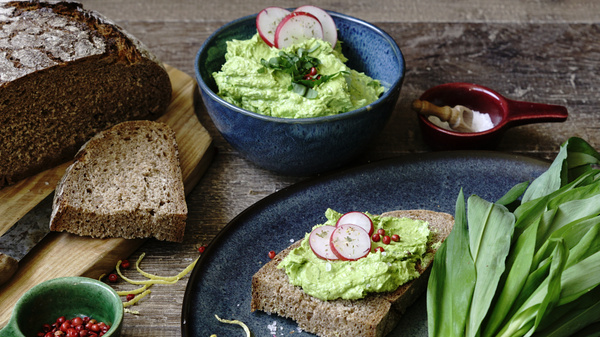 KI generiert: Brot mit Bärlauchaufstrich, garniert mit Radieschenscheiben, dazu frisches Brot und Bärlauchblätter.