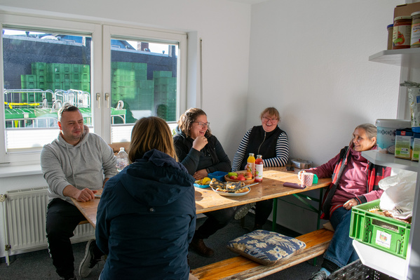 KI generiert: Fünf Personen sitzen an einem Tisch und unterhalten sich in einem Zimmer mit Fenstern und Regalen.