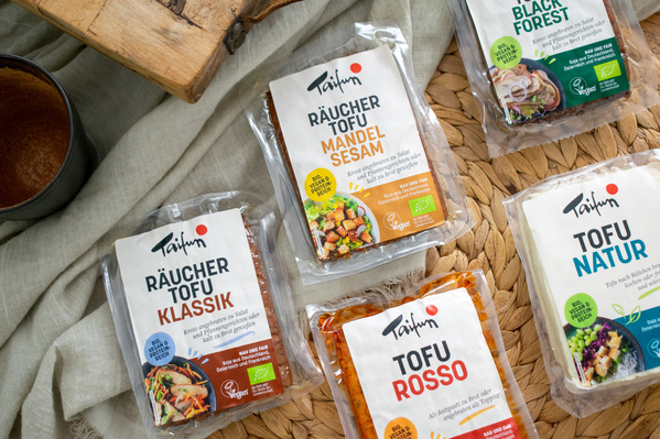 KI generiert: Verschiedene Taifun-Tofu-Produkte auf einem Tisch arrangiert, darunter "Räucher Tofu Mandel Sesam".