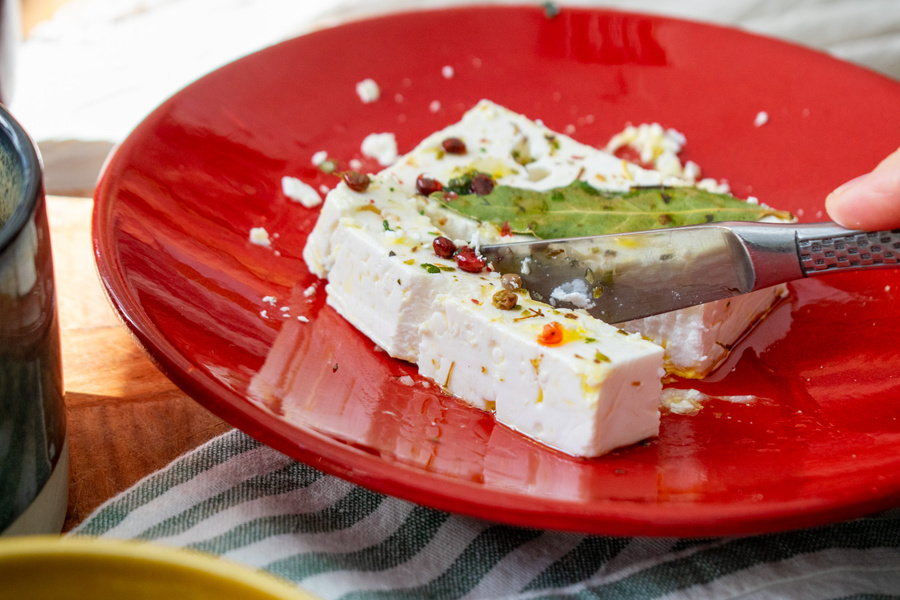 KI generiert: Ein Stück Feta mit Kräutern und Gewürzen auf einem roten Teller.