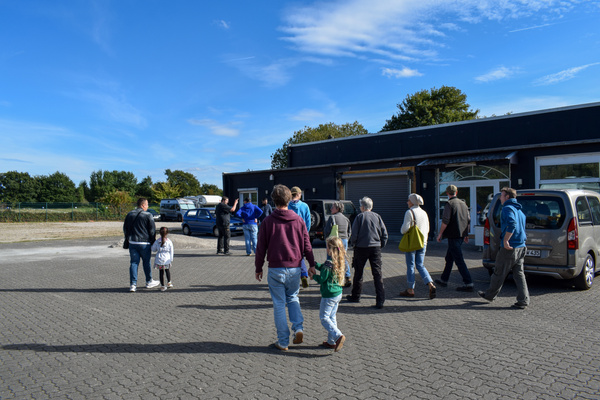 KI generiert: Gruppe von Menschen geht über den Parkplatz eines Gebäudes bei klarem Himmel.