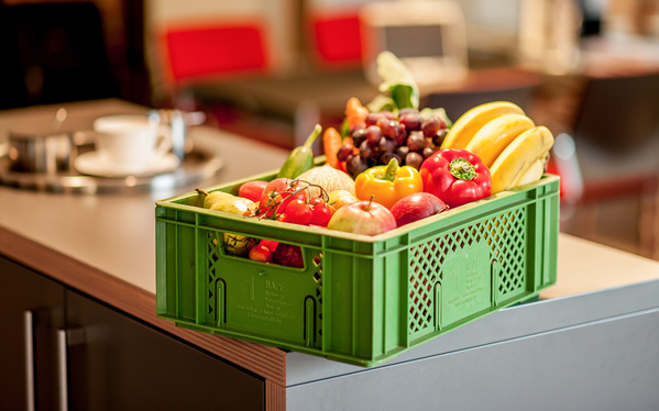 KI generiert: Grüne Kiste voller frischem Obst und Gemüse steht auf einem Tisch in einem modernen Raum.