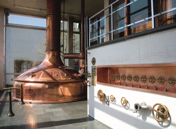 KI generiert: Großer, kupferner Braukessel in einer Brauerei mit Ventilen an der Wand.