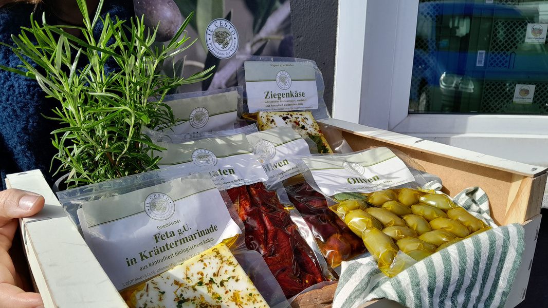 KI generiert: Eine Holzkiste mit Ziegenkäse, Feta und Oliven, daneben ein Kräutertopf.