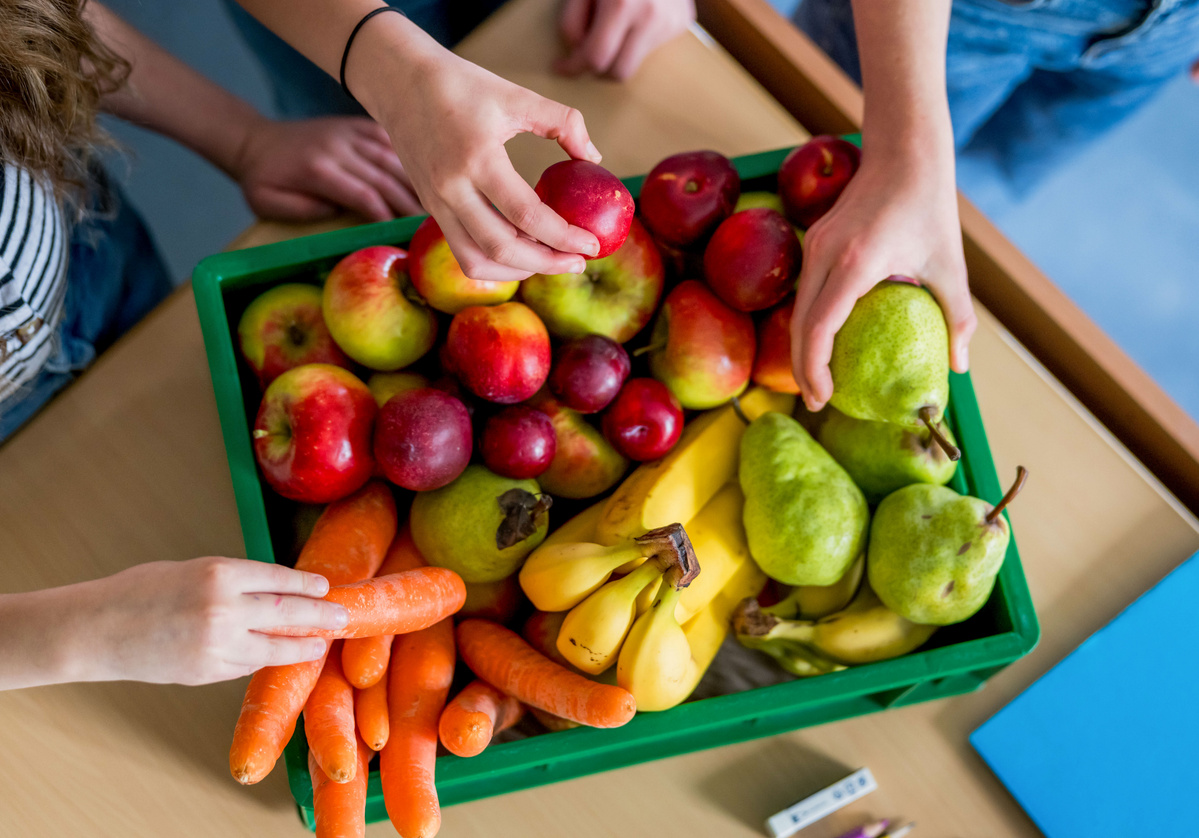 KI generiert: Eine grüne Kiste voller Obst und Gemüse, darunter Äpfel, Bananen, Birnen und Karotten. Hände greifen danach.
