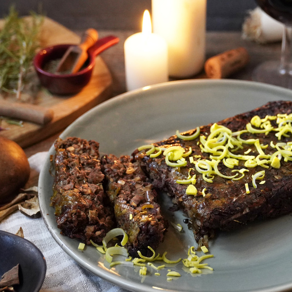KI generiert: Ein Teller mit einem veganen Braten, garniert mit Frühlingszwiebeln, neben brennenden Kerzen.