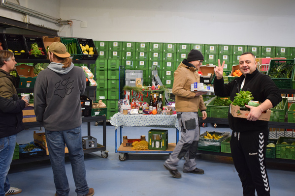 KI generiert: Mehrere Personen sortieren Obst und Gemüse in einer Lagerhalle. Eine Person zeigt das Peace-Zeichen.