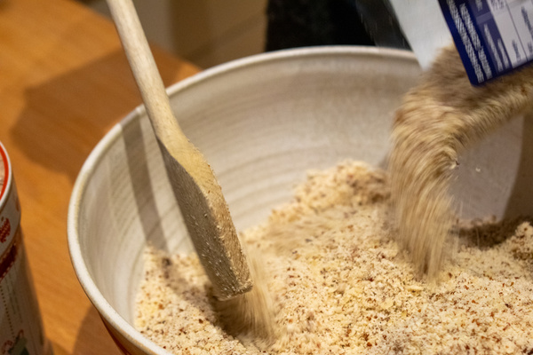 KI generiert: Jemand gibt gemahlene Mandeln in eine Schüssel und rührt mit einem Holzlöffel um.