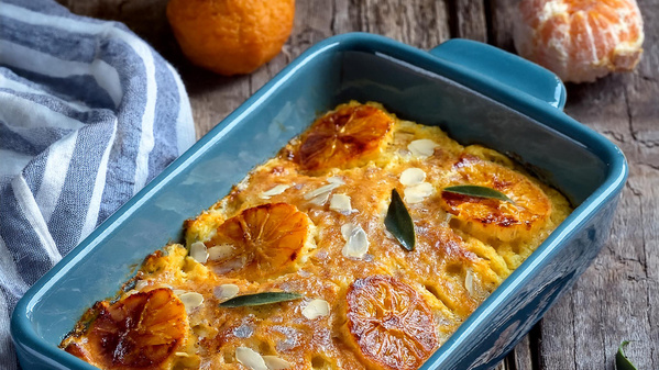 KI generiert: Ein gebackenes Gericht mit Orangen in einer blauen Auflaufform, umgeben von einer Serviette und Orangen.