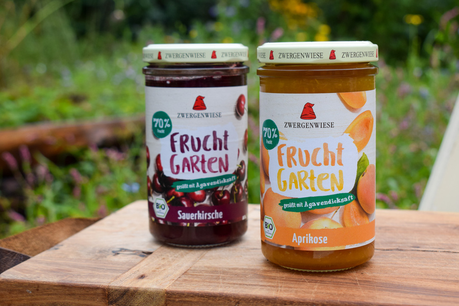 KI generiert: Zwei Marmeladengläser auf einem Tisch, Sorten Sauerkirsche und Aprikose, mit Etikett "Frucht Garten".