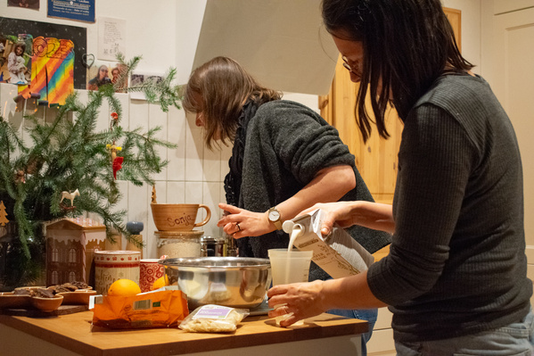 KI generiert: Zwei Personen backen in einer Küche; eine gießt Milch in einen Becher.