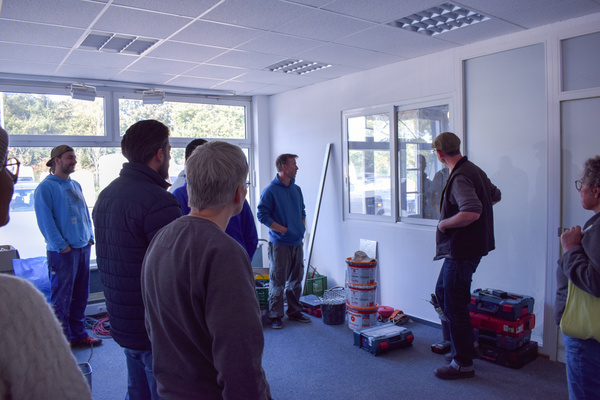 KI generiert: Personengruppe diskutiert in einem Raum voller Werkzeuge und Baumaterialien.