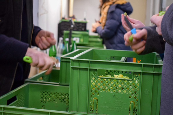 KI generiert: Menschen packen Gemüse in grüne Kisten in einem Lagerraum.