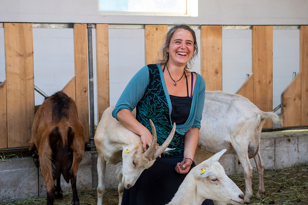 KI generiert: Eine lachende Frau in einem Stall mit mehreren Ziegen.