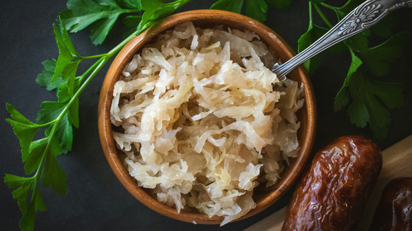 KI generiert: Schüssel mit Sauerkraut und einer Gabel, daneben frische Petersilie und Würste.