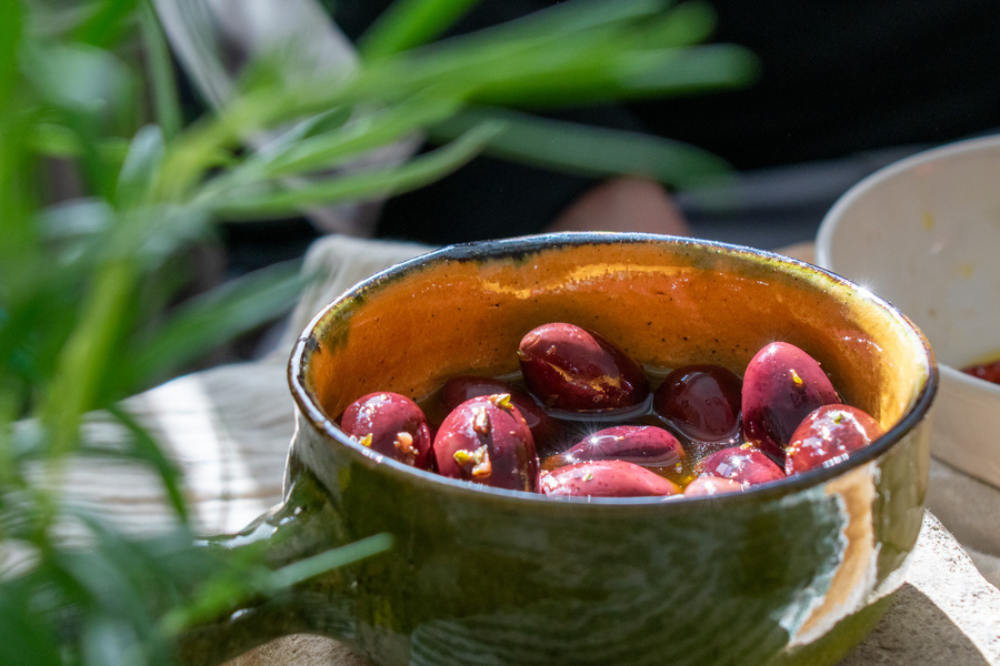 KI generiert: Schale mit eingelegten Oliven, umgeben von grünen Pflanzen im Tageslicht.