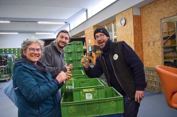KI generiert: Drei Personen stehen lächelnd bei grünen Kisten, vermutlich in einem Lagerraum.