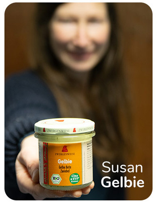 KI generiert: Eine Frau hält ein Zwergenwiese-Glas mit "Gelbie" in der Hand. Text: "Susan Gelbie".