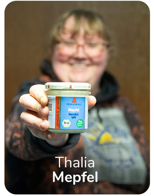 KI generiert: Eine Person hält ein Glas mit der Aufschrift "Zweckliese Mepfel". Text: "Thalia Mepfel".