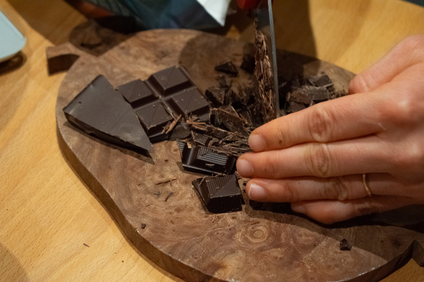 KI generiert: Hand schneidet Zartbitterschokolade auf einem Holzbrett.