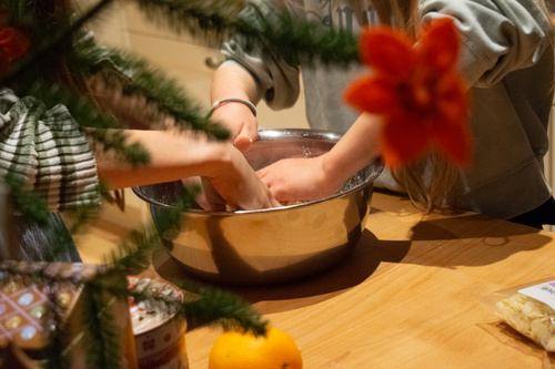 KI generiert: Zwei Personen kneten Teig in einer Schüssel auf einem Holztisch, dekoriert mit einem Weihnachtsstern.