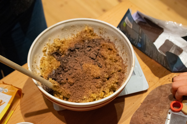 KI generiert: Eine Rührschüssel mit Kuchenteig und Schokoladenstücken auf einem Holzbrett.