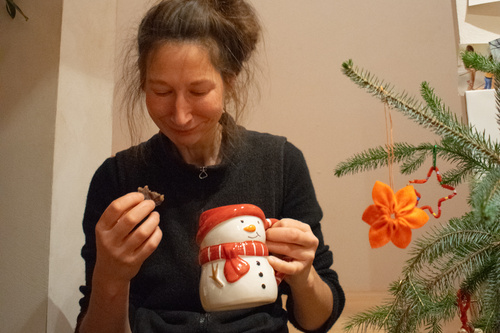 KI generiert: Eine Person mit einer Schneemann-Tasse und Gebäck neben einem geschmückten Zweig.