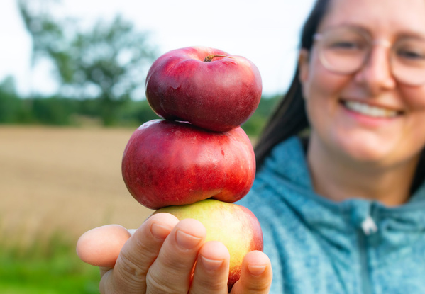KI generiert: Frau balanciert drei Äpfel auf der Hand und lächelt.