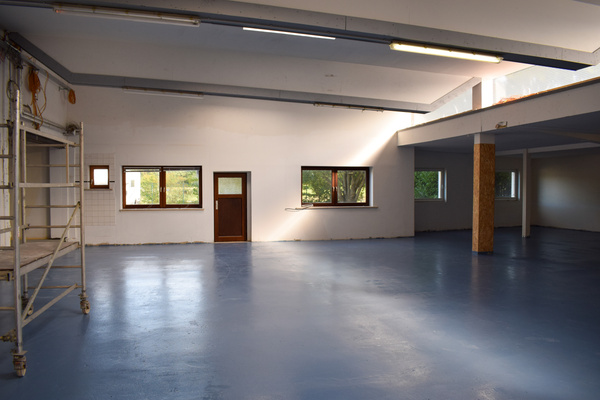 KI generiert: Geräumiger Innenraum mit blauem Boden, leeren Wänden und einem Gerüst links.