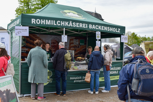 KI generiert: Leute stehen an einem Verkaufsstand der Rohmilchkäserei Backensholz. Text: "KARTENZAHLUNG möglich".