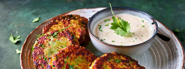 KI generiert: Zucchini-Puffer auf einem Teller mit Dip, garniert mit Kräutern.