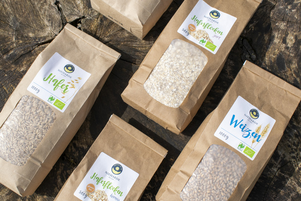 KI generiert: Verschiedene Verpackungen von Bio-Hafer und -Weizen auf Holzhintergrund. Text: "Hafer", "Haferflocken", "Weizen".