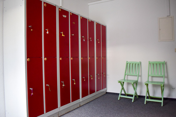 KI generiert: Rote Schließfächer und zwei grüne klappbare Stühle in einem Raum.