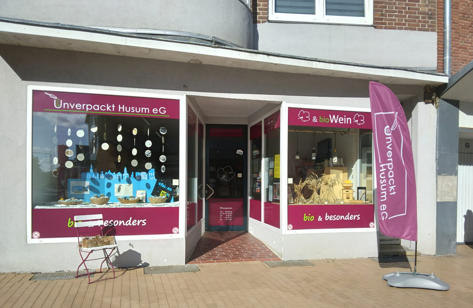 KI generiert: Ein Laden namens "Unverpackt Husum eG" mit Auslage und Werbung für Bio-Produkte und Wein.