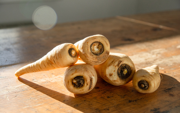 KI generiert: Fünf Pastinaken liegen auf einem Holztisch im Sonnenlicht.